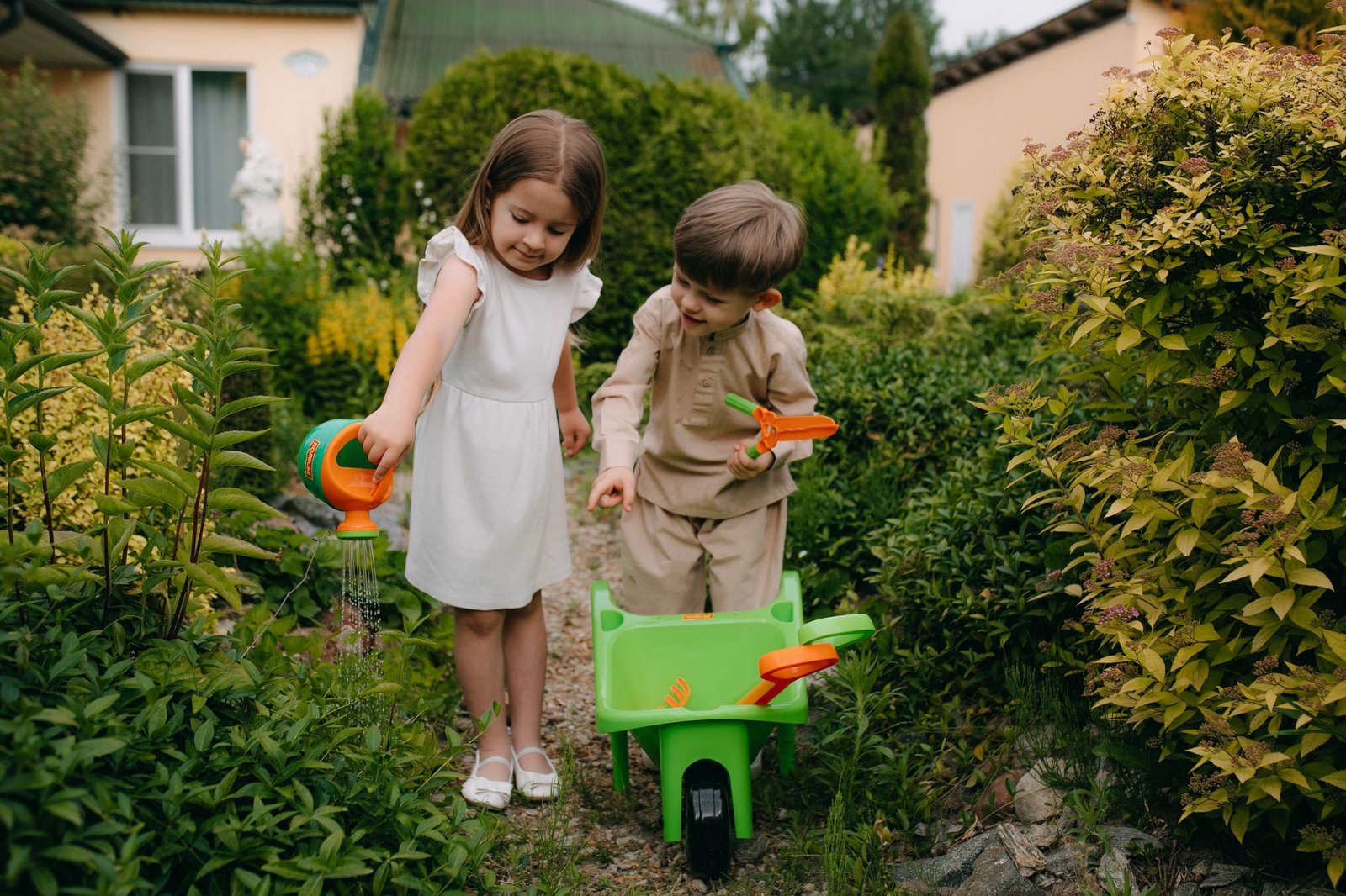 Zwei Kinder spielen mit einer Schubkarre im Garten