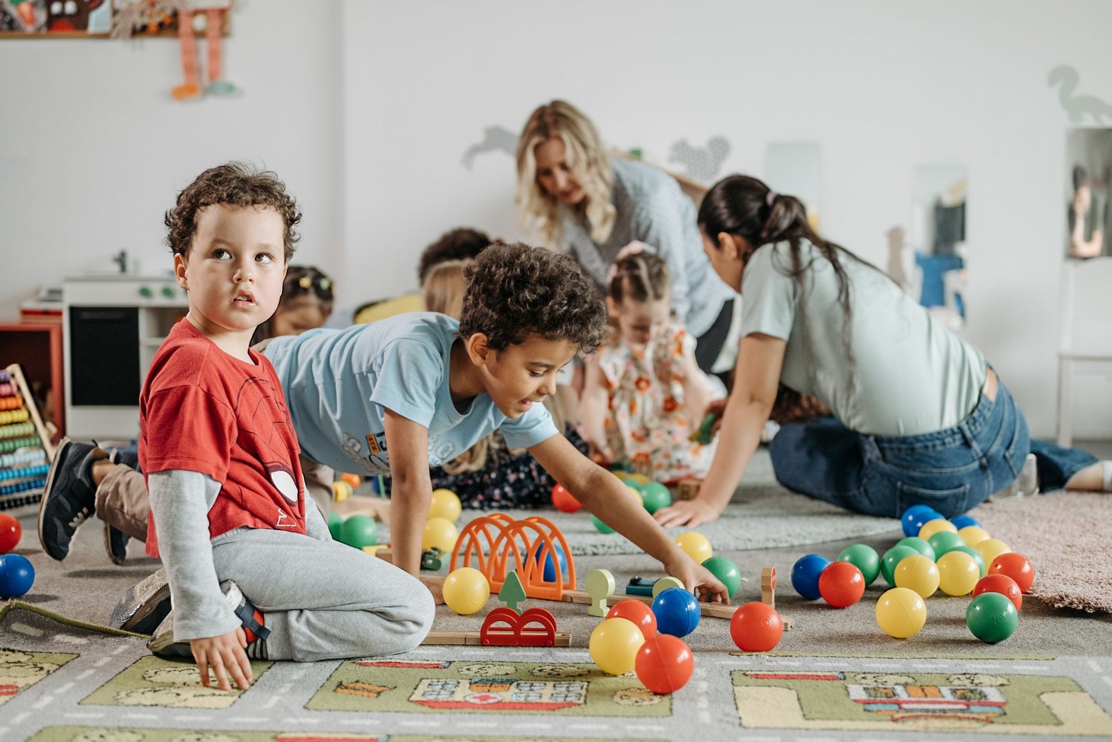 Kinder spielen mit Erzieherinnen auf dem Boden im Gruppenraum