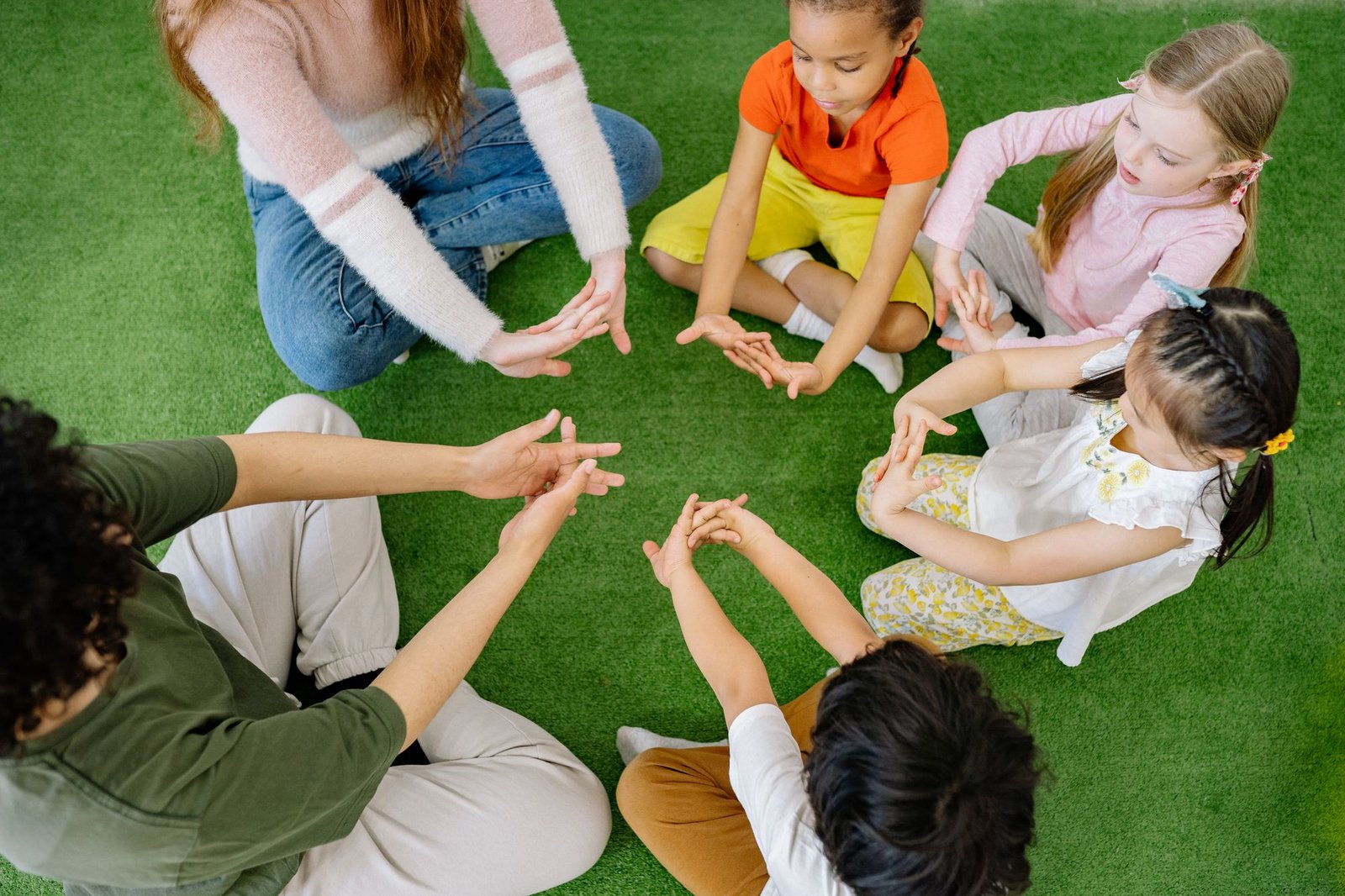 Kinder und Erzieherinnen sitzen im Kreis auf dem Boden